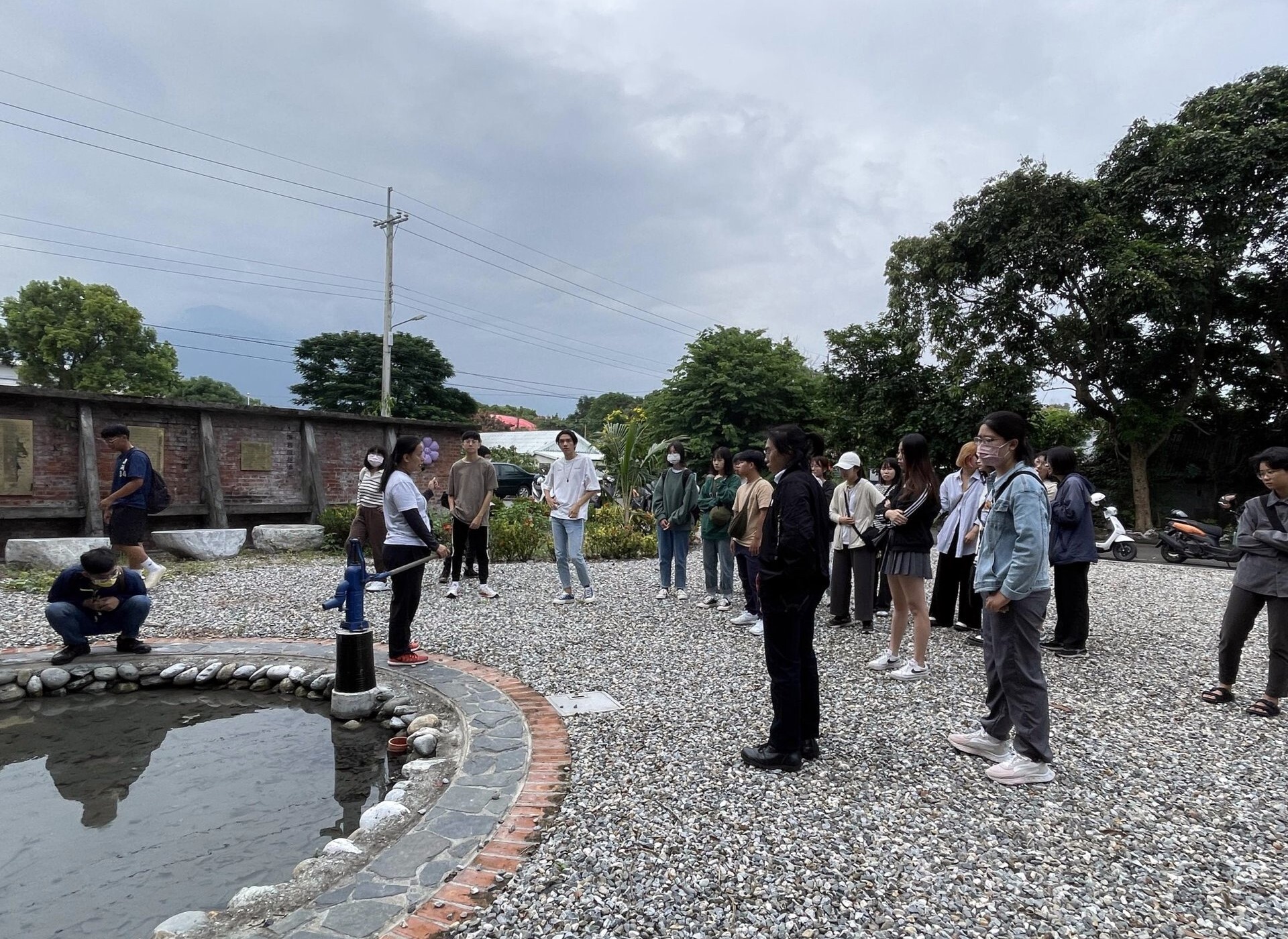 師生聽取林家菱監事介紹生之泉,後方紅磚建築為昔日的蓄水設施