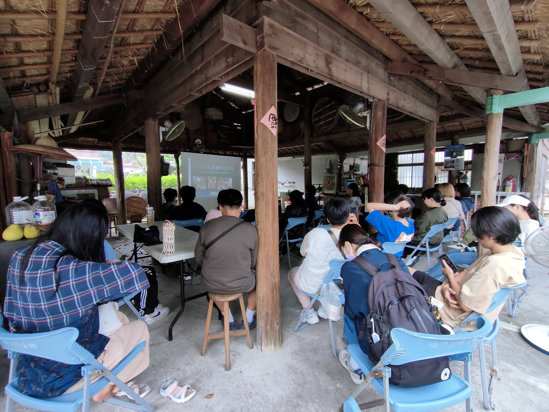師生在傳統茅草屋下聽取簡報