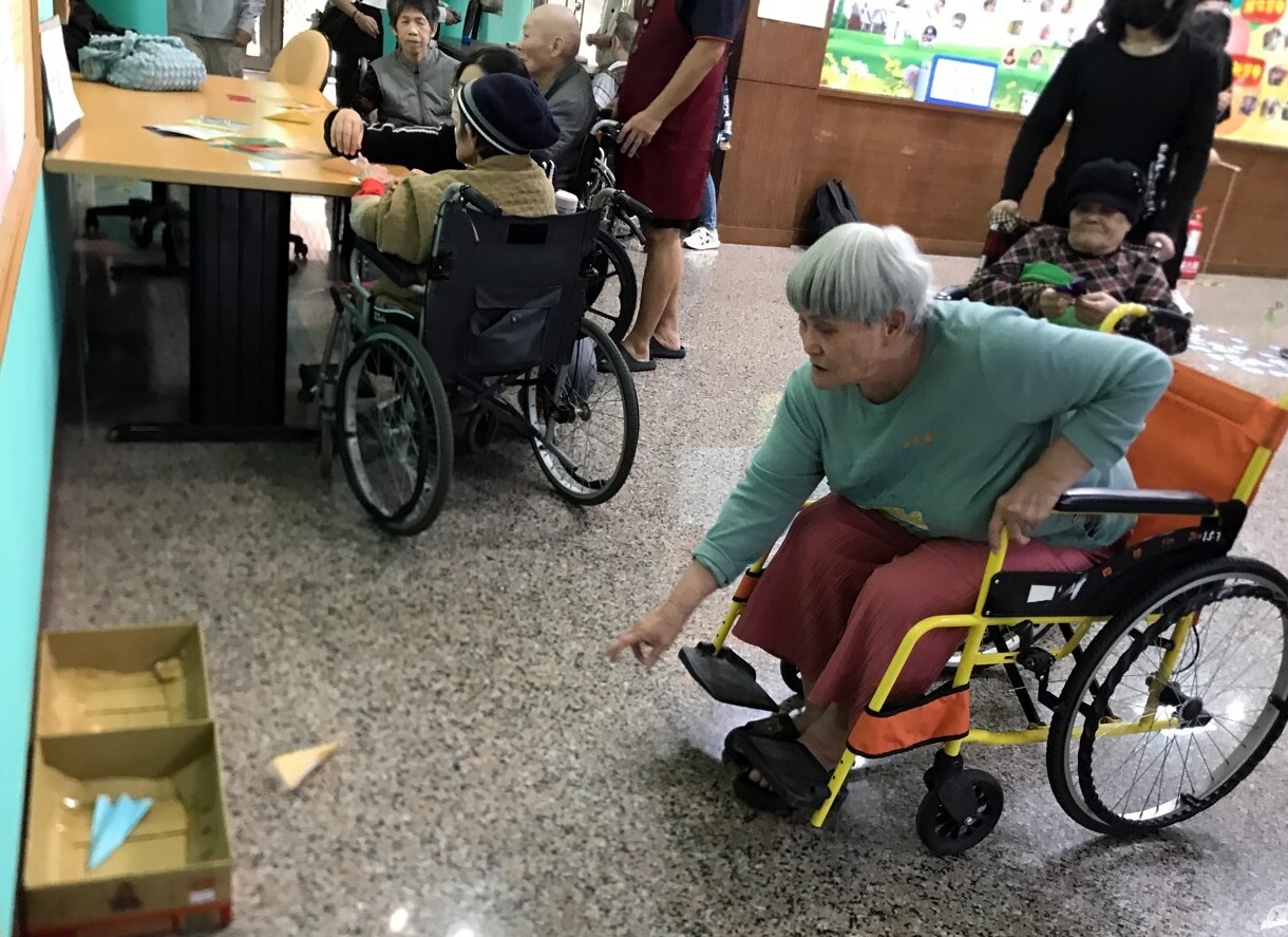 長者把自己折好的紙飛機用力朝紙箱投去,左上角為折紙飛機區