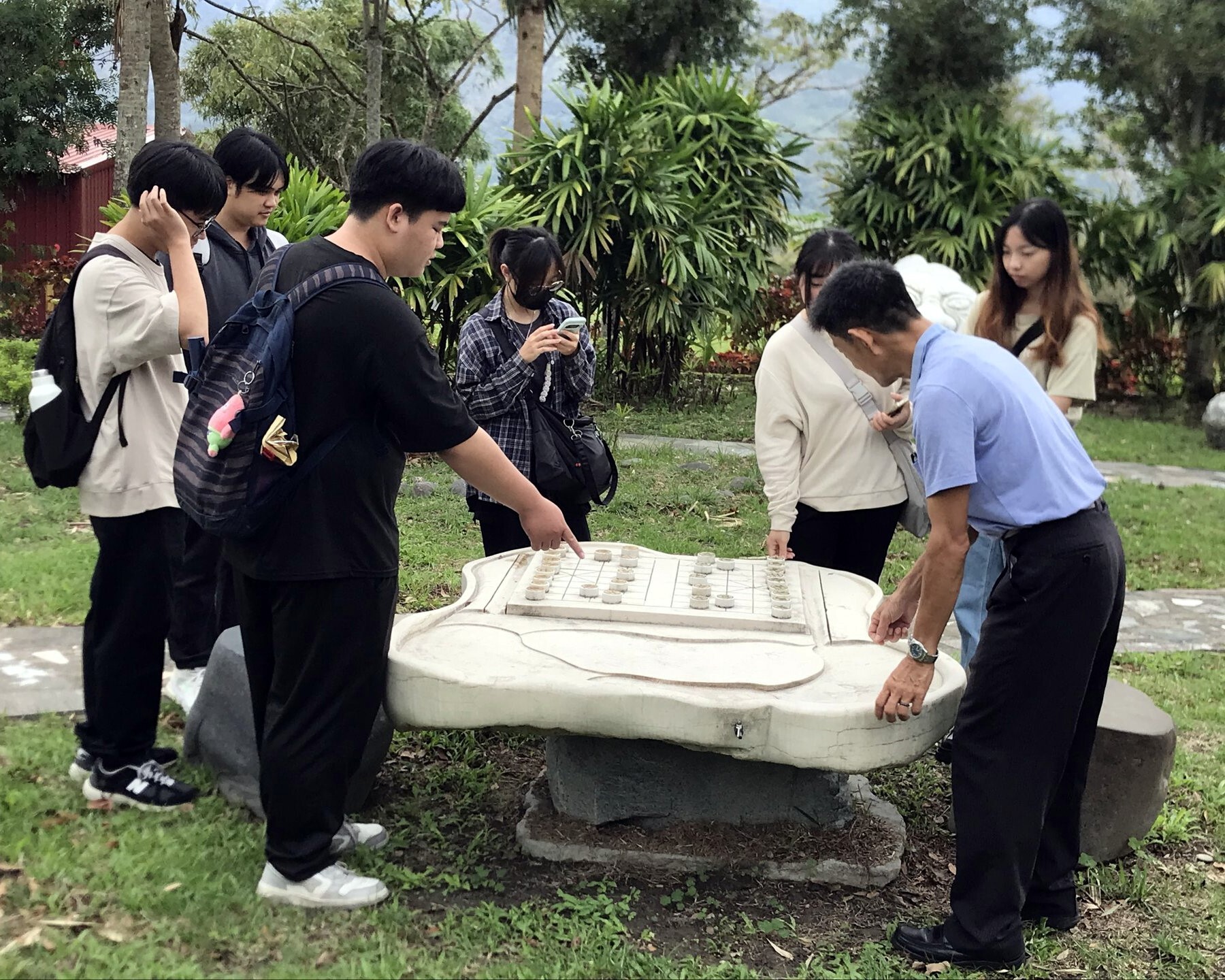 曾富良科長(右側著淺藍色上衣者)跟學生介紹這個由一整塊石材雕成的茶盤及象棋,鼓勵學生玩玩看