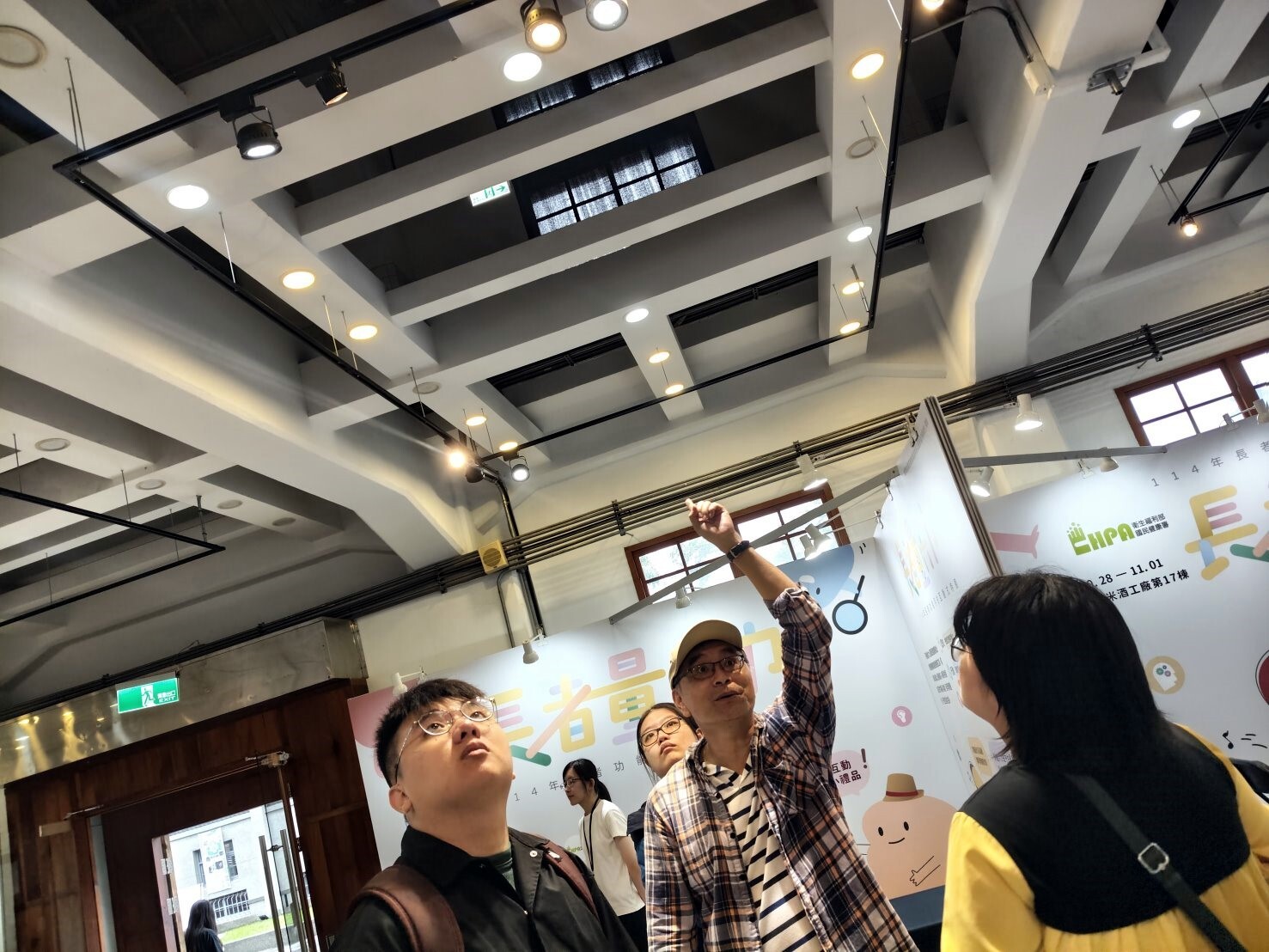 老師帶領學生觀察舊酒廠修復木造房時增添的鋼骨結構,背景為廠商舉辦展覽